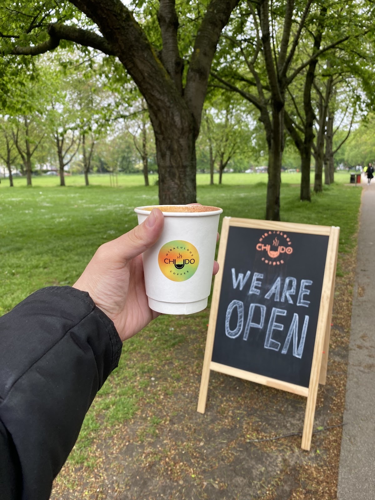 A white takeaway cup held in front of the park lawn